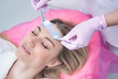 Cosmetician hands spreading blue clay over woman forehead with two cosmetic brushes